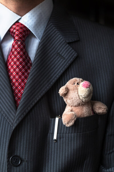 Элегантный стильный бизнесмен держит милого плюшевого медведя в кармане нагрудного костюма. Формальная концепция переговоров
.