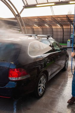 A black car being washed at a self-service car wash, covered in water and suds, as part of its cleaning process.