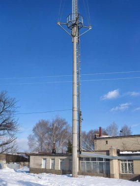 A tall communication tower stands prominently, next to a building, contrasting the clear blue sky on a sunny winter day with snowy ground.