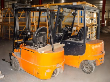 Forkliftler malzeme taşımaya hazır. Arkasında tahta sandıklar var. Bu da yoğun bir endüstriyel ayar olduğunu gösteriyor.