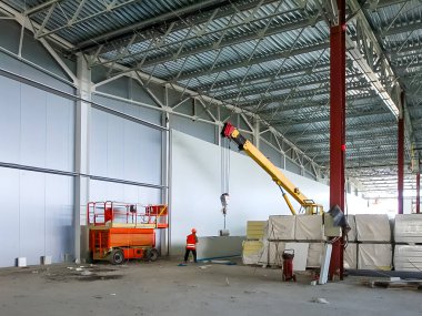 Bir inşaat işçisi, büyük bir endüstriyel binaya malzeme yerleştirilmesini denetliyor.