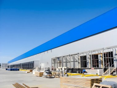 Çoklu yükleme bölmeleri olan büyük bir dağıtım merkezi parlak, bulutsuz bir gökyüzü altında gösterilir