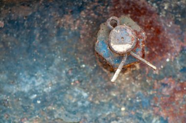 Üzerinde mavi ve turuncu ipuçları olan desenli, eski metalik bir arka plana karşı aşınmış bir kulübe pimi ve cıvata başlığının ayrıntılı görüntüsü