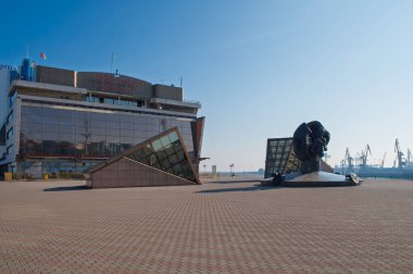 Odesa, Ukrayna. 3 Ekim 2016. Cam ön cephesi ve geometrik şekilleriyle Odesa Deniz Terminali 'nin modern mimarisi, arka planda endüstriyel vinçlerle görülebilen eşsiz bir heykel ile birlikte.