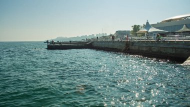 Odesa, Ukrayna. 3 Ekim 2016. İnsanlar Odesa seti boyunca berrak mavi gökyüzünün altında pırıl pırıl deniz ve uzak şehir siluetiyle geziniyor.