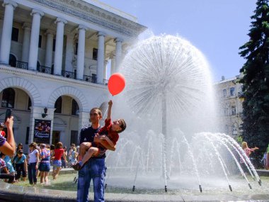 Kyiv, Ukrayna. 28 Mayıs 2011. Bir baba heyecanlı oğlunu şehir meydanında büyük, küresel bir çeşmenin yanında kırmızı bir balon tutarak kaldırır.