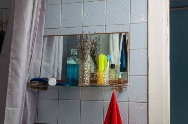 Ağız gargarası, diş fırçası ve parfüm şişeleri gibi çeşitli kişisel bakım malzemelerini içeren, dokuma vazoda kurutulmuş lavanta içeren bir banyo rafının yakından görüntüsü.