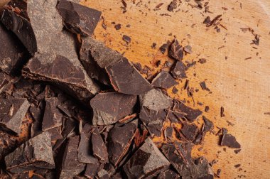 Koyu çikolata parçalarının ve ahşap bir tahtanın üzerindeki ince talaşların yakın çekim görüntüsü hoşgörü ve sanatsal hazırlık duygusunu çağrıştırıyor.
