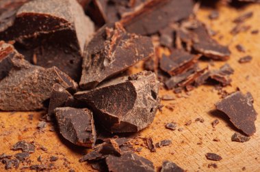Kaba desenli kırık çikolata parçalarının yakın plan görüntüsü, ahşap bir yüzeye yayılmış, pişirme veya şekerleme ima ederek