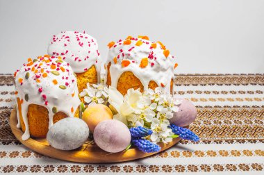 Şenlikli bir Paskalya sofrası, renkli yumurtalar ve desenli masa örtüsü üzerindeki narin bahar çiçekleriyle çevrili özenle dekore edilmiş kulich kekleri içerir.