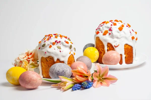 Kulich olarak bilinen iki güzel dekore edilmiş Paskalya pastası, temiz beyaz arka planda canlı boyanmış yumurtalar ve narin bahar çiçekleriyle sunuluyor.