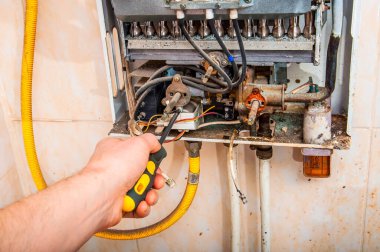 Bir teknisyenin elinin arızalı bir gaz ısıtıcı ünitesinin karmaşık kabloları ve boruları üzerinde çalışırken yakın plan çekimi.