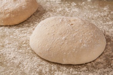 Un tozuyla kaplı iki raunt çiğ pizza hamuru un kaplı bir yüzeye oturmuş, pişirmeye hazır.