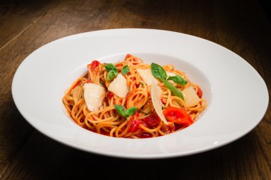 Beyaz bir tabak spagetti domates, parmesan ve fesleğen ile hizmet