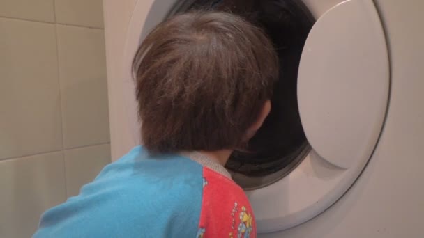 Мальчик смотрит на свою одежду в стиральной машине — стоковое видео