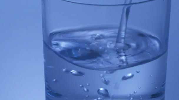 Llenar un vaso con agua sobre fondo azul — Vídeo de stock