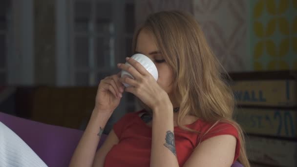 Mooie jonge vrouw drinken van thee in leunstoel en glimlachen. — Stockvideo