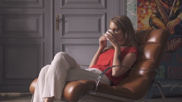 Hermosa mujer joven con taza de té sentado en el sillón en casa . — Vídeos de Stock