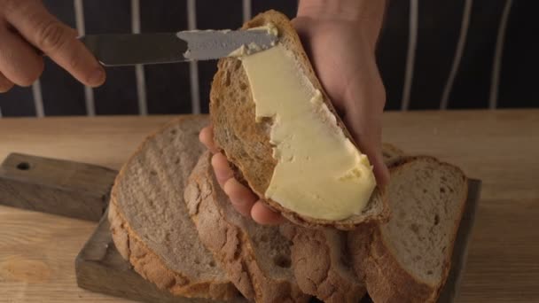 Ręką człowieka ściera masło na kawałek chleba żytniego — Wideo stockowe