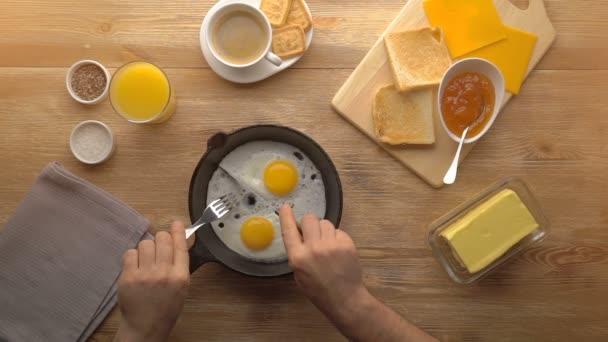 Male hands cut the fried eggs on black pan, top view — Stock Video