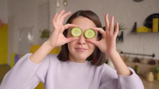 Funny mix race asiática chica bailando en la cocina y disfrutando de la comida en casa, divirtiéndose mientras prepara ensalada hacer caras divertidas cubrir los ojos con círculos de pepino. Cocina saludable comida vegana cocept — Vídeos de Stock