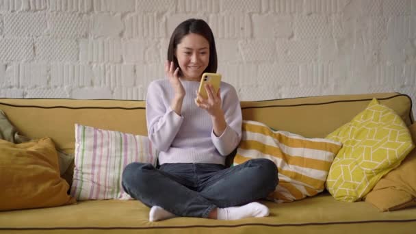 Amazed happy asian girl celebrating getting ecommerce shopping sale offer on smartphone at home. Excited mixed race customer winner looking at mobile phone using app celebrating mobile victory concept — Stock Video