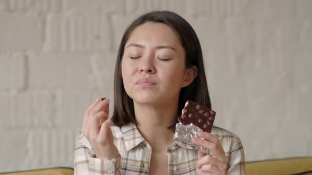 Asiatisk blandras glad ung kvinna njuter av att äta välsmakande bar nötter choklad med glädje hemma, närbild porträtt — Stockvideo