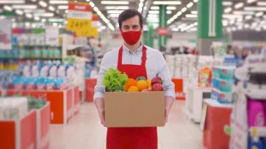Maskeli ve üniformalı teslimatçı markette karton kutuda sebzelerle duruyor, salgın sırasında teslimat servisinde çalışan kurye, koronavirüs salgını, çevrimiçi gıda alışverişi