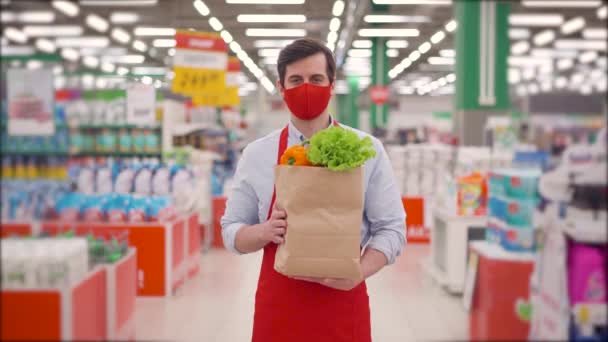 Mężczyzna sklep kurier w masce twarzy stojący w supermarkecie z warzywami w opakowaniu papierowym, dostawca pracujący w usłudze dostawy podczas epidemii covid-19, pandemia koronawirusa, zakupy online żywności — Wideo stockowe