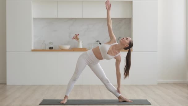 Junge attraktive multiethnische Frau trägt weiße Sportbekleidung, Hose und Oberteil, macht Stretching-Yoga-Übungen auf Fitnessmatte im Wohnzimmer, Gesundheits- und Bewegungstherapie zu Hause — Stockvideo