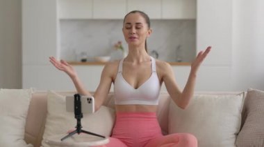 Genç çok ırklı yoga koçu, oturma odasında yoga pranayama pratiği yapıyor, kişisel video blogu için online akış eğitimi dersi kaydediyor, web kamerası eğitim konsepti