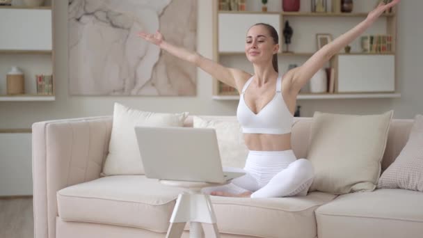 Mindful atraente jovem mista mulher procurando laptop prática de ioga curso on-line sentado no sofá confortável em casa. Menina milenar pacífica profundamente meditando, fazendo exercícios de ioga respiração — Vídeo de Stock