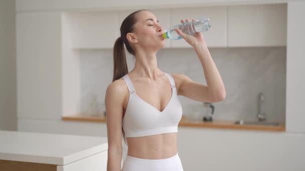Fit saine sportive mixte race jeune femme tenir bouteille boire de l'eau claire minérale fraîche après l'entraînement de remise en forme exercice à la maison, actif belle fille en vêtements de sport garder l'équilibre d'hydratation — Video