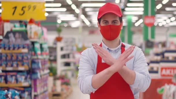 Jonge verkoper man in de supermarkt draagt rode masker tonen verbod hand gebaar aandringen om thuis te blijven op quarantaine. Coronavirus mers covid 19 bescherming. Stop het concept van de verspreiding van corona-virussen. — Stockvideo