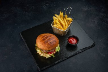 Koyu masada patates kızartması ve bir kase domates soslu taze hamburger.