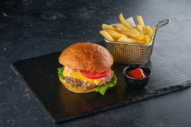 Koyu masada patates kızartması ve bir kase domates soslu taze hamburger.