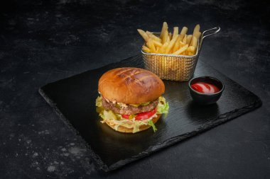 Koyu masada patates kızartması ve bir kase domates soslu taze hamburger.