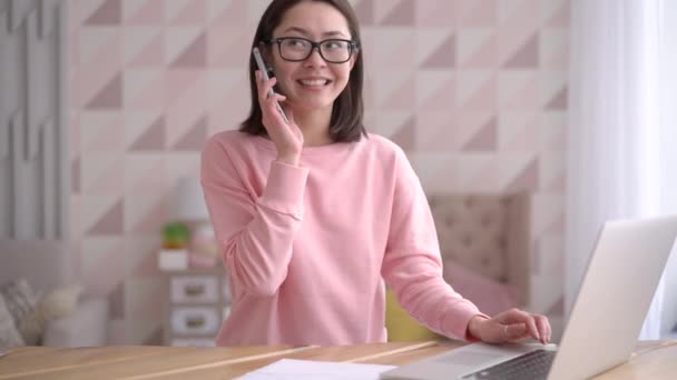 Pozytywny młody wieloetniczny kobieta biznesu rozmawia przez telefon za pomocą laptopa siedzieć w biurze w domu biurko, szczęśliwy azjatycki klient kobieta wykonać telefon komórkowy potwierdzając online zakupy koncepcji dostawy zamówienia — Wideo stockowe