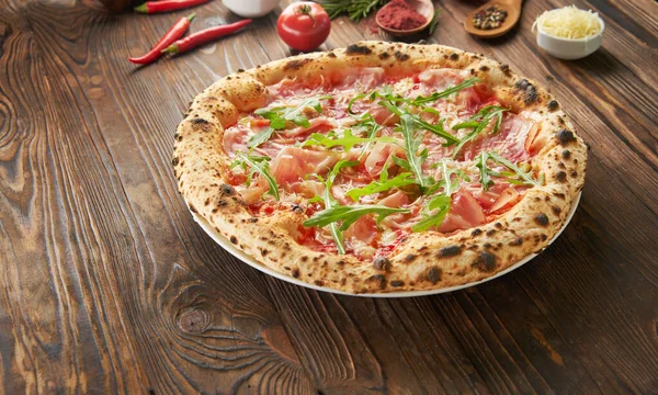 Parma jambonlu ve ahşap zemin üzerinde taze roka bulunan orijinal İtalyan Napoli pizzası. Fast food yeme konsepti