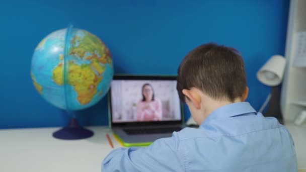 Rapaz da escola primária bonito usando computador portátil aprendizagem em casa. Miúdo fofo focado assistindo vídeo aula estudando na mesa, fazendo lição de casa. Crianças educação remota sobre conceito de quarentena. — Vídeo de Stock