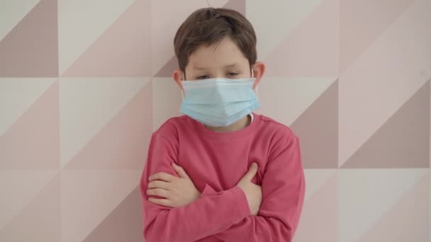 Petit écolier portant un masque médical en regardant la caméra ayant coronavirus covid 19 maladie du virus respiratoire se sent la peur, se tient à la maison. Gros plan portrait, concept de sécurité et de protection — Video