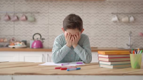 Verärgerter kleiner Junge frustriert über Hausaufgaben, trauriger müder Schüler, der seinen Kopf mit beiden Händen hält und zu Hause seine Hausaufgaben macht, Konzept des Fernunterrichts — Stockvideo