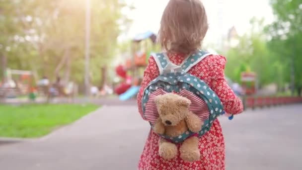 Sırt çantasında oyuncakla şehir parkında yürüyen sevimli küçük kız. Çocuk bakımı ve aktif çocuk konsepti — Stok video