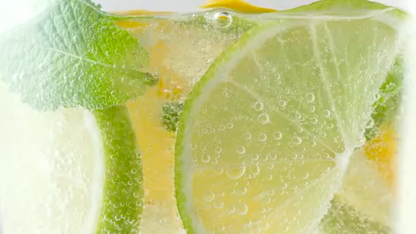 Cool refreshing homemade summer lemonade in a glass with ice cubes and fresh mint leaves. Lemon slice in fizzy sparkling soda with bubbles, juice refreshment citrus carbonated soft drink or beverage — Stock Video