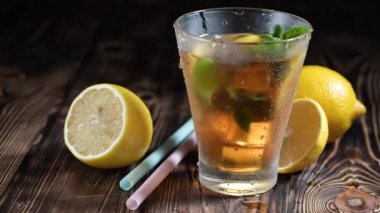 Bir bardak buzlu çay ve dilimlenmiş limon. Köy ahşap zemininde taze nane. Detoksifikasyon için sağlıklı ferahlatıcı limonata, yaz mevsimi için tatlı tatlı, yumuşak, soğuk, aromatik içecek.