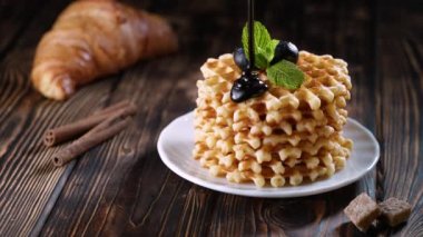 Eritilmiş çikolatayı yaban mersinli ve beyaz tabakta nane şekerli yeni pişmiş Belçika wafflelarının üzerine döküyorum. Tahta masada ya da kırsal arka planda kahvaltı için nefis ev yapımı hamur işi.