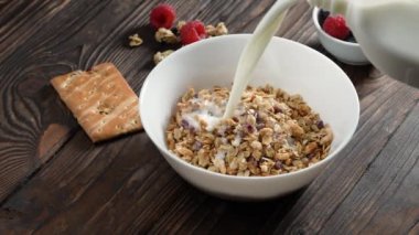 Beyaz kaseye müsli gevrekleri ile birlikte süt dökmek. Kırsal ahşap arka planda kahvaltı. Sağlıklı granola, temiz yemek, vejetaryen diyeti, alerji dostu, sabah enerjisi, kilo verme konsepti.