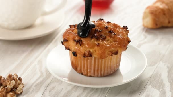 Despeje molho de chocolate extra escuro derretido ou xarope no bolo de muffin caseiro em câmera lenta. Biscoito doce, pastelaria caseira, textura líquida sobre fundo de madeira branca — Vídeo de Stock