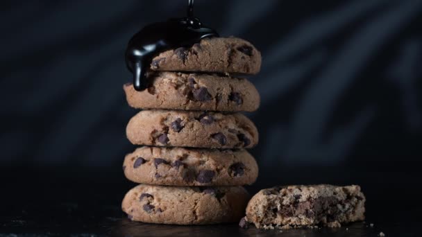 Verter extra oscuro derretido salsa de chocolate líquido sobre la pila de galletas caseras en cámara lenta. Galletas dulces, pastelería casera, textura líquida sobre fondo negro — Vídeos de Stock