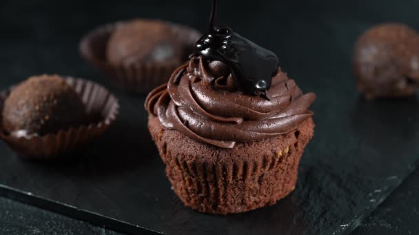 Giet extra donker gesmolten chocoladesaus over een heerlijke, smakelijke cupcake in slow motion. Zoete koekjes, zelfgebakken gebak, op donkergrijze zwarte leisteen achtergrond of textuur — Stockvideo